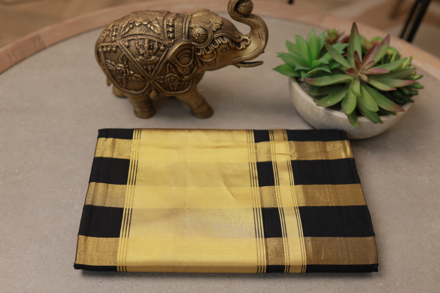 The Pure Handloom Black & Gold Striped Kerala Saree folded, showing the gold kasavu border and black checks
