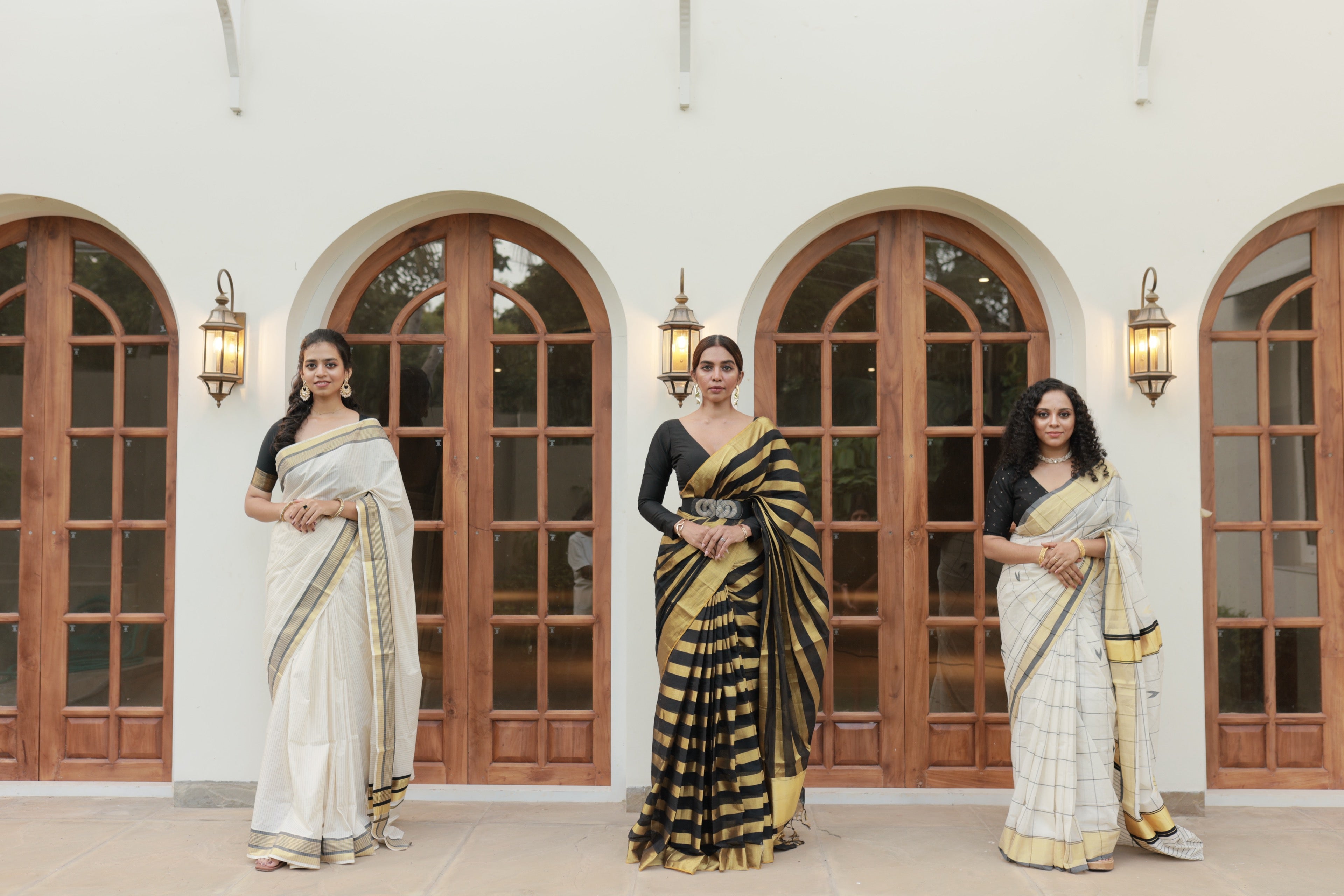 Three models wearing Alaypayuthe handloom sarees, standing before an arched colonial-style doorway